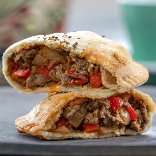 Two Big E Cafe empanadas, cut in half, revealing a savory filling of ground meat, red peppers, and onions.