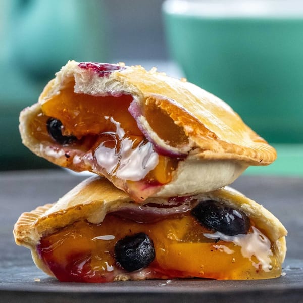 Two fruit empanadas, one stacked atop the other, revealing a filling of peaches and blueberries.