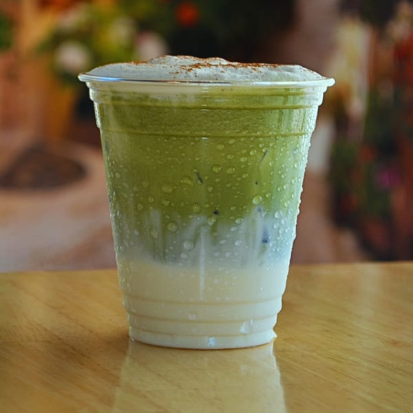Iced matcha latte with whipped cream and cinnamon in a plastic cup on a wooden table.