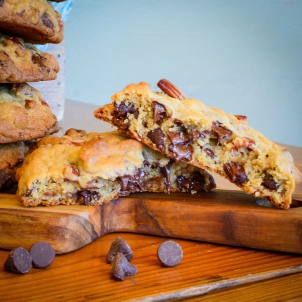 A stack of chocolate chip cookies with one broken in half, revealing gooey chocolate and nuts.