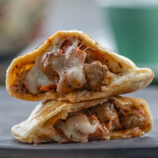 Two Big E Cafe empanadas, cut open to reveal melted cheese and savory sausage filling, stacked.
