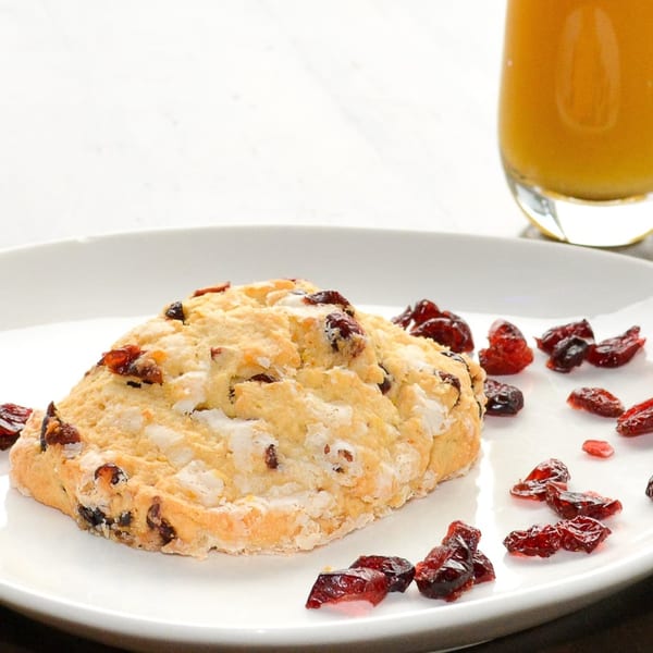 A cranberry scone with dried cranberries on a white plate, with a glass of orange juice.